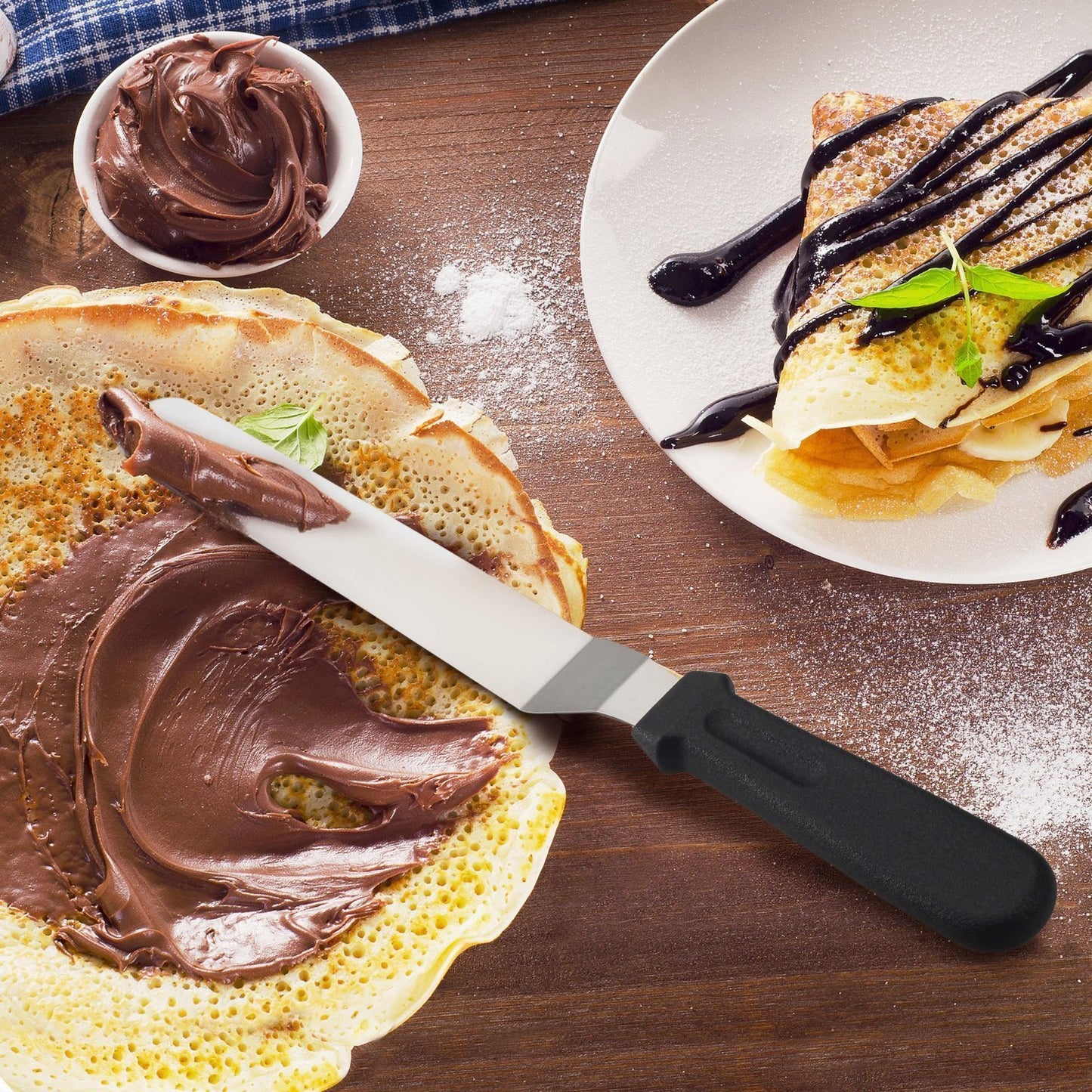 Crepe being spread with chocolate cream on a wooden surface