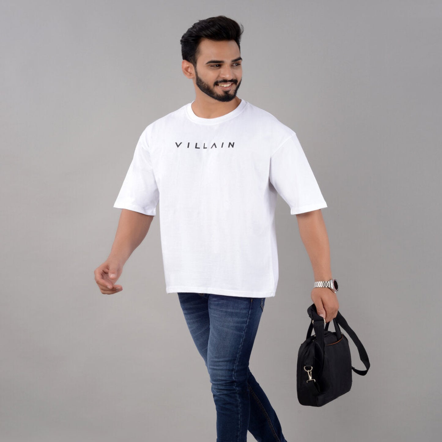 Man wearing a white t-shirt with 'VILLAIN' text, holding a black bag on a gray background
