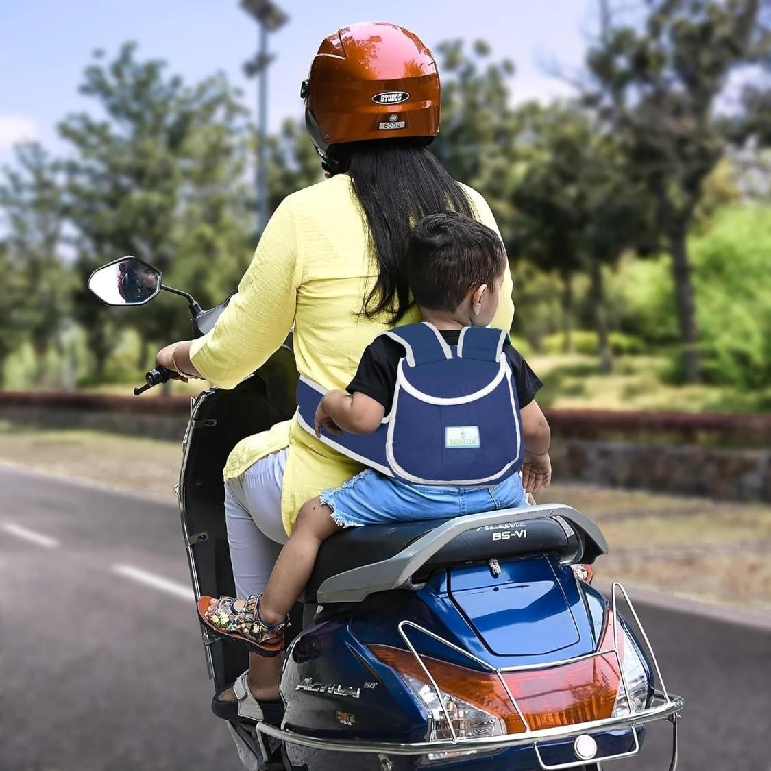 Woman and child riding a scooter with a child safety seat on a road.