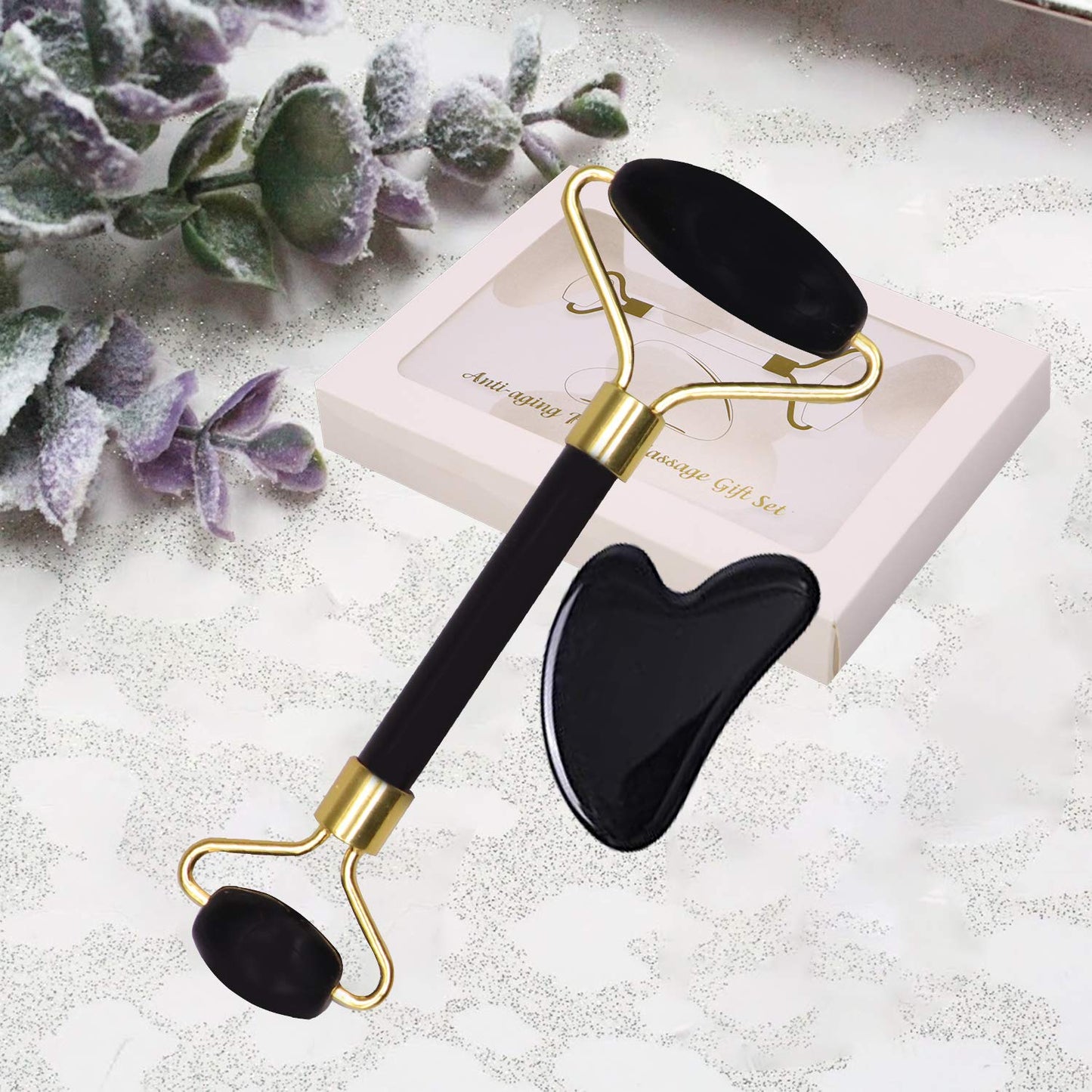 Black and gold facial roller and gua sha tool on a white surface with decorative elements.