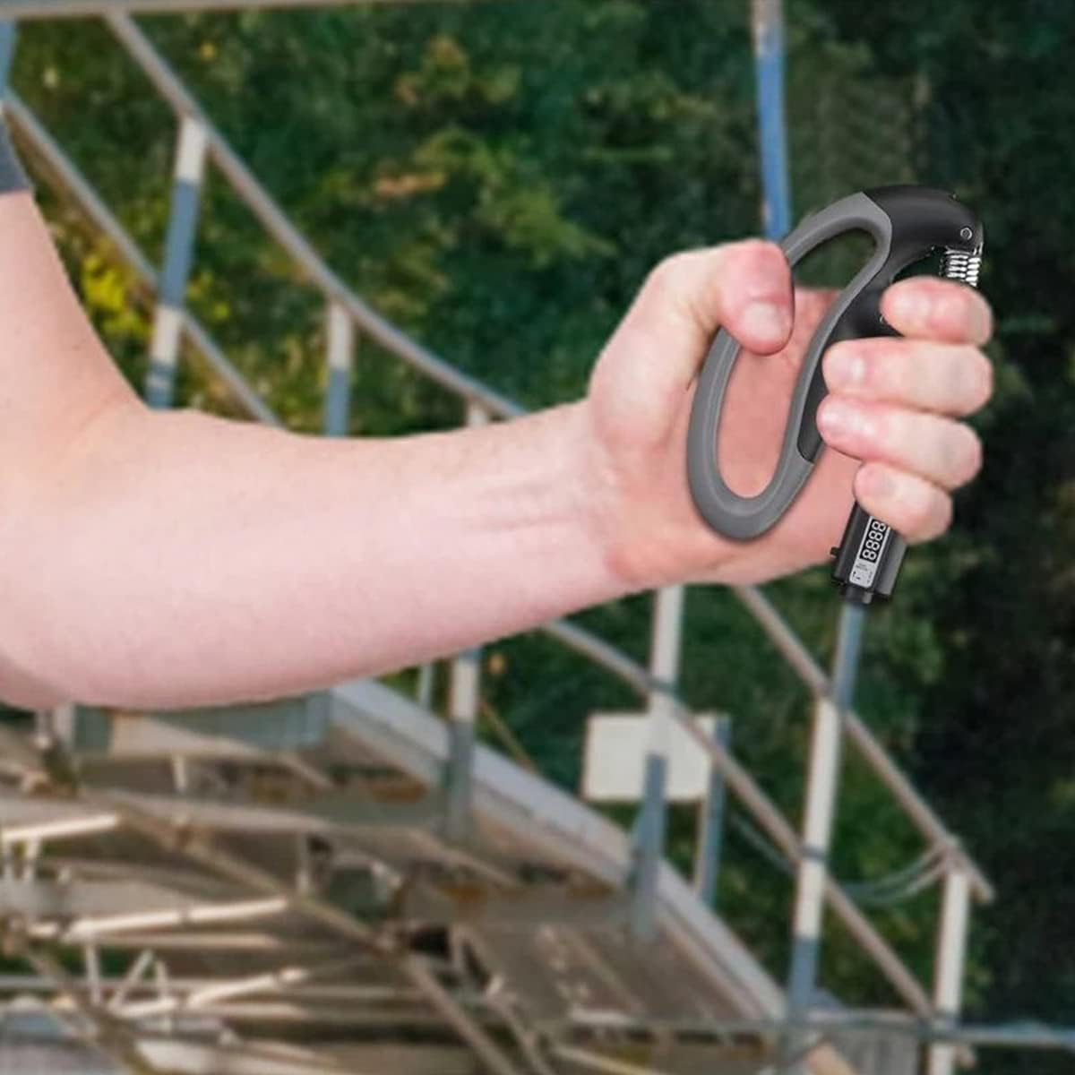 Hand holding a black carabiner with a blurred background of trees and metal structures
