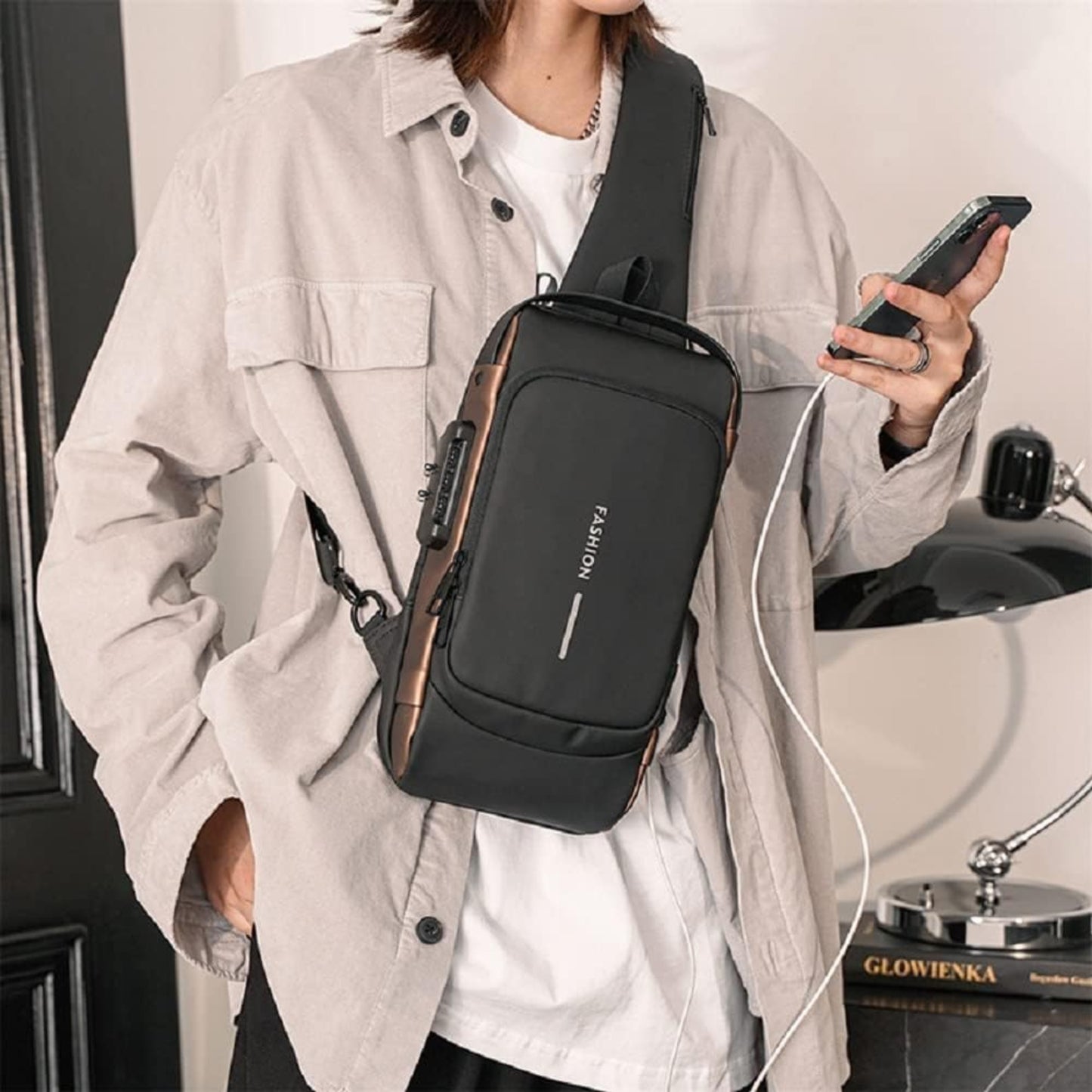Person wearing a black crossbody bag holding a phone, with a neutral background
